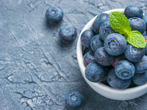 Freshly picked blueberries closeup. Ripe and juicy fresh blueberry with green mint leaves on textured concrete background. Bilberry on gray background with copyspace. Top view or flat lay