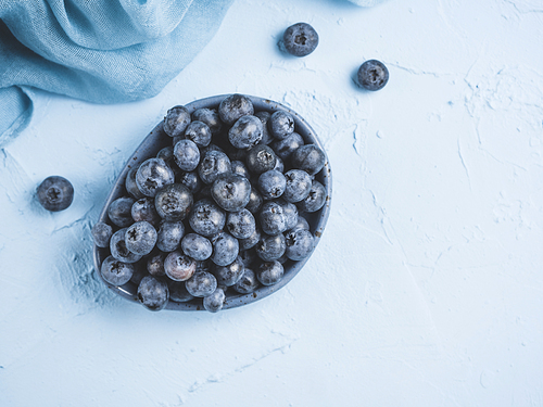 Blueberries in plate on blue background. Fresh picked bilberries close up. Copyspace. Top view or flat lay