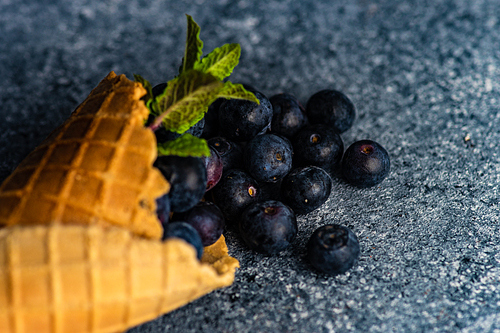 Organic blueberry fruits in waffle cone on concrete background with copy space