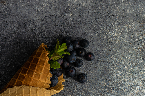 Organic blueberry fruits in waffle cone on concrete background with copy space