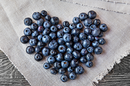 Blueberry heart lie on a homespun tablecloth on wooden background. Rustic cozy background with healthy food. Fresh-gathered berries full of vitamins, good for diet nutrition and healthy meals.