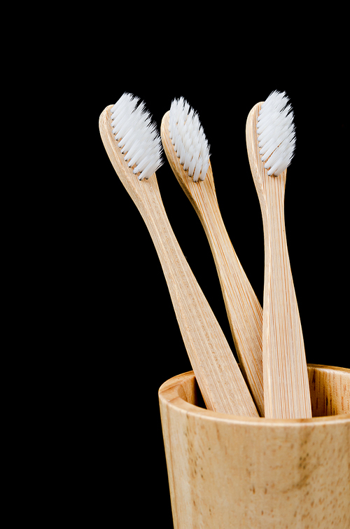 Bamboo toothbrushes in wooden cup on black background, Zero waste concept.