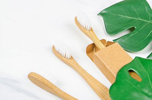 Bamboo toothbrushes with green leaves on marble background. Zero waste concept.