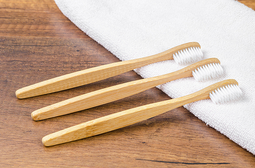 Bamboo toothbrushes with towel on wooden background. Eco friendly concept.