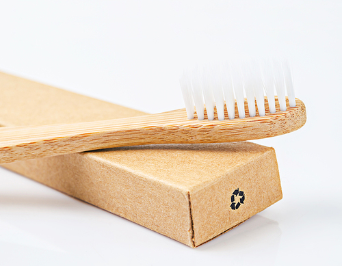 Bamboo toothbrushes on brown paper box with recycle sign on white background.