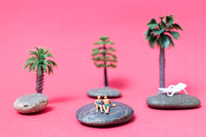 Miniature people wearing swimsuit relaxing on the rock with pink background , Valentine's day concept