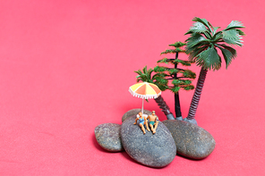 Miniature people wearing swimsuit relaxing on the rock with pink background , Valentine's day concept