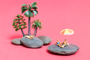 Miniature people wearing swimsuit relaxing on the rock with pink background , Valentine's day concept