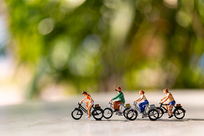 Miniature people  ride a  bicycle outdoors with green bokeh background , sport and travel  concept