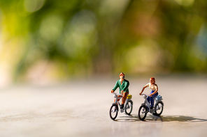 Miniature people  ride a  bicycle outdoors with green bokeh background , sport and travel  concept