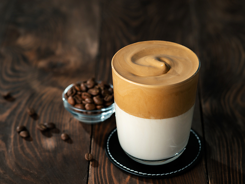 Trendy korean drink - dalgona coffee. Glass jar with cold or hot beverage - whipped instant coffee with milk and coffee beans on brown wooden background with copy space for text or design