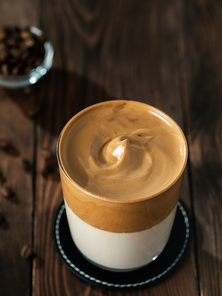 Trendy korean drink - dalgona coffee. Glass jar with cold or hot beverage - whipped instant coffee with milk and coffee beans on brown wooden background with copy space for text or design. Vertical