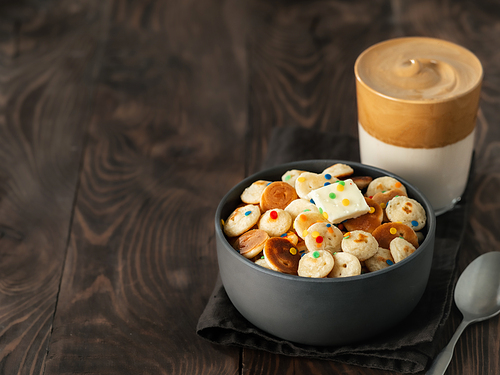 Mini pancakes cereal and dalgona coffee on brown wooden background, copy space. Trendy food and drink - tiny panckakes served sprinkles and whipped instant coffee with milk or korean dalgona coffee