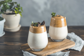 Two glasses with water drops of Dalgona frothy coffee trend korean drink latte espresso with coffee foam, decorated by thyme and dark chocolate. Dark wooden table surface