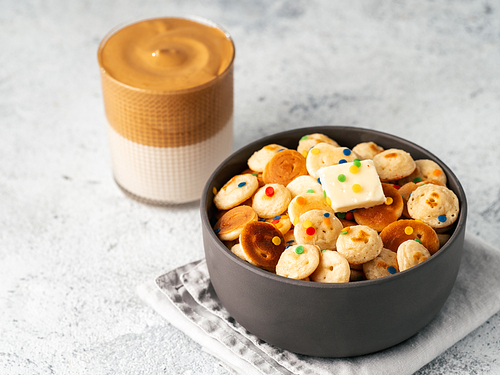 Mini pancakes cereal and dalgona coffee on gray cement background, copy space. Trendy food and drink - tiny panckakes served sprinkles and whipped instant coffee with milk or korean dalgona coffee