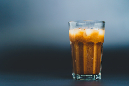 Ice coffee in a tall glass on dark background.