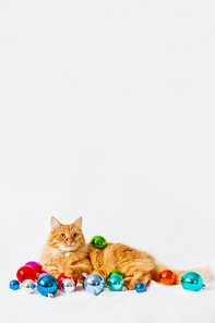 Cute ginger cat lies among christmas decorations - bright colorful balls. The fluffy pet comfortably settled to sleep or to play. Cute cozy holiday background, morning bedtime at home. Place for text.