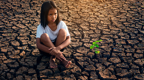 Sad girl  sitting on dry soil with small trees that grow beside him. Concept climate change, global warming, water crisis, World environment and pollution.