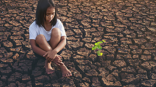 Sad girl  sitting on dry soil with small trees that grow beside him. Concept climate change, global warming, water crisis, World environment and pollution.