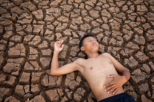 Sad a boy Lying  on cracked earth waiting for the hope of the sky to rain. Affected of global warming made climate change. Water shortage and drought concept.