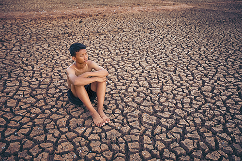 Sad a boy sitting on cracked earth waiting for the hope of the sky to rain. Affected of global warming made climate change. Water shortage and drought concept.
