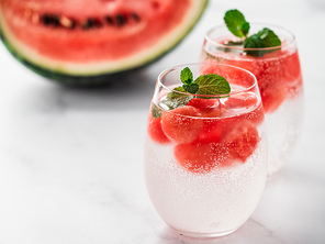 Watermelon ice with sparkling water or soda in glass tumbler. Summer party idea and recipe, add color and flavor for soda or other drink. Copy space. White marble background