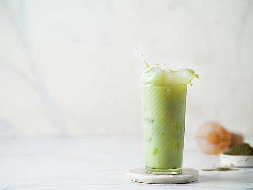 Homemade iced matcha latte with splashes on white marble background. Copy space for text or design