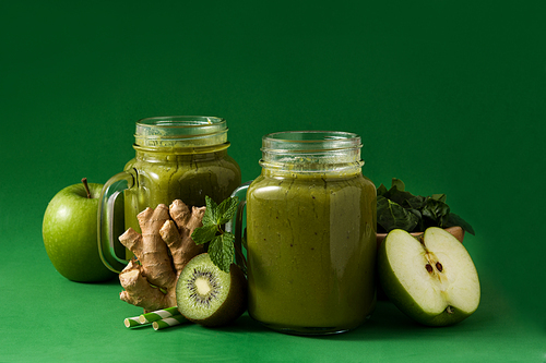 Healthy green smoothie in jar on green background