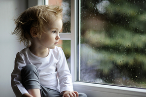 Adorable toddler girl looking at raindrops on the window