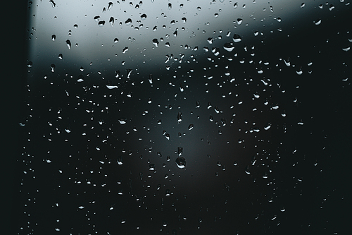 A horizontal background of some moody rain drops over a window with dark tones and textured droplets