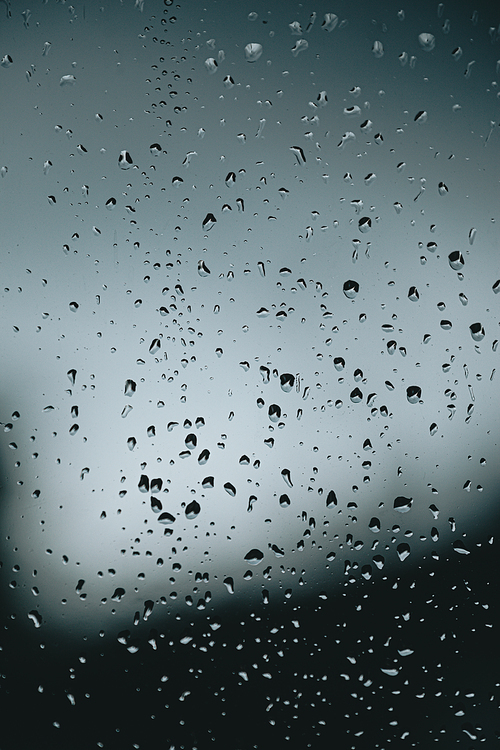 A vertical background of some moody rain drops over a window with dark tones and textured droplets