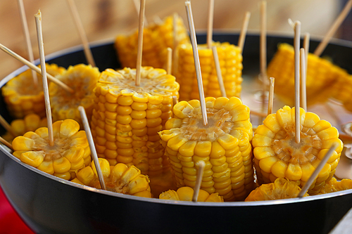 Closeup ready to eat boiled or steamed sweet corn cobs on stick in a big cooking pan, high angle view