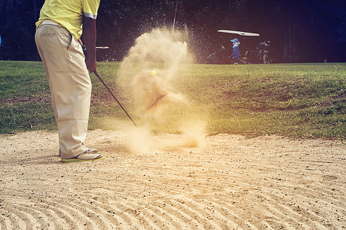Golfer hitting the ball on the sand to stay on the green. Speeds Cause blurred by movement
