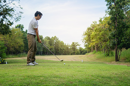 Man playing golf on beautiful sunny green golf course. Hitting golf ball down the fairway from the tee with driver. Golfer hitting ball with club on beatuiful golf course