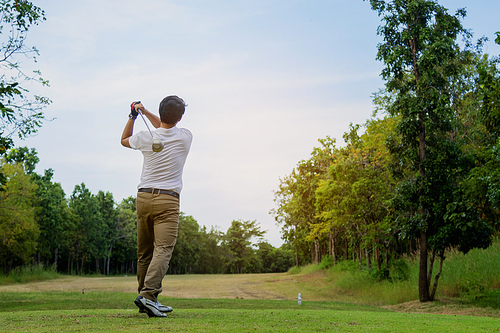 Man playing golf on beautiful sunny green golf course. Hitting golf ball down the fairway from the tee with driver. Golfer hitting ball with club on beatuiful golf course