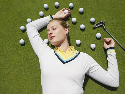 Young woman lying on green surrounded with golf balls view from above