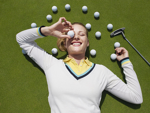 Young female golfer lying on green holding ball in front of eye view from above