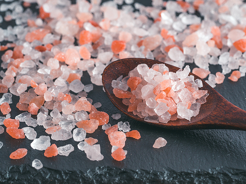 Himalayan pink salt in spoon on black stone background. Copy space