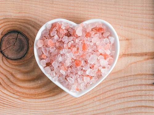 Himalayan pink salt in hearth-shape bowl on wooden background. Copy space