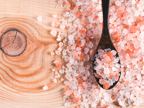 Himalayan pink salt in spoon on wooden background. Copy space
