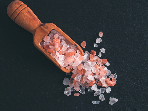 Himalayan pink salt in wooden scoop on black stone background. Copy space