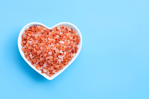 Pink himalayan salt in heart shape bowl on blue background. Copy space