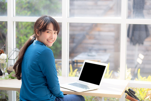 Beautiful of portrait asian young woman sitting looking camera and laptop on desk at coffee shop, professional female freelance working notebook computer connect internet online job, business concept.