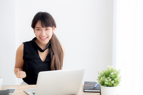 Beautiful portrait asian young woman smile working online laptop computer with happy satisfied sitting on desk office, girl using notebook with excited and glad, business and success concept.