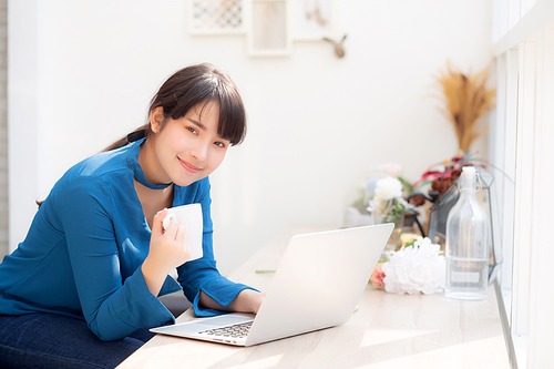 Beautiful young freelance asian woman smiling working and on laptop computer at desk coffee shop with professional, asia girl using notebook and drink coffee, business and lifestyle concept.