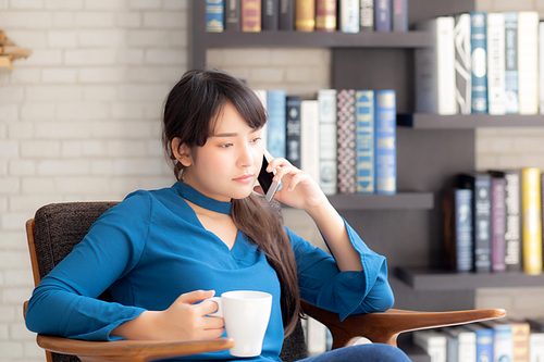 Beautiful portrait young asian woman smiling using mobile smart phone talking enjoy and drink coffee with relax, girl sitting on chair at living room, communication concept.