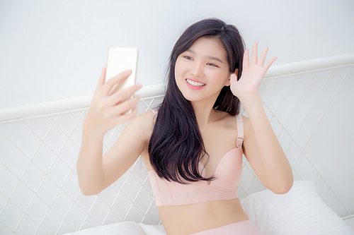 beautiful young asian woman  in underwear talking a selfie on smartphone for social network in the bedroom, girl in lingerie relax with taking a picture on mobile phone on bed in the bedchamber.