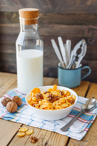 Tasty corn flakes with walnuts in bowl with bottle of milk. Rustic wooden background with plaid napkin. Healthy crispy breakfast snack.