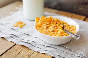 Tasty corn flakes in bowl with bottle of milk. Rustic wooden background with homespun napkin. Healthy crispy breakfast snack.