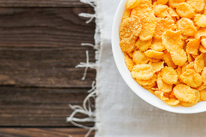 Tasty corn flakes in bowl. Rustic wooden background with homespun napkin. Healthy crispy breakfast snack. Top view, flat lay. Place for text.